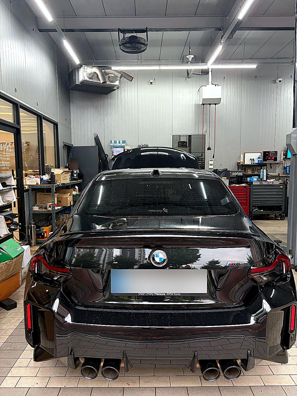 정비 공장 안에 세워진 BMW M2 후면, M2 배지와 배기구 네 개