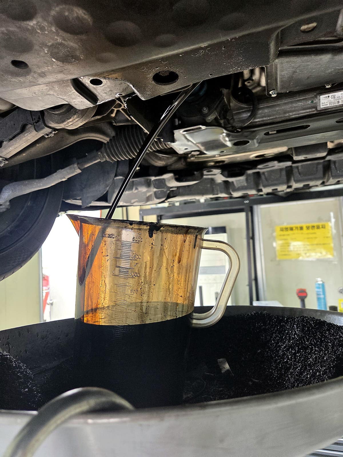 벤츠 S63 AMG 하부에서 검게 변한 폐엔진오일을 계량컵에 배출하는 모습