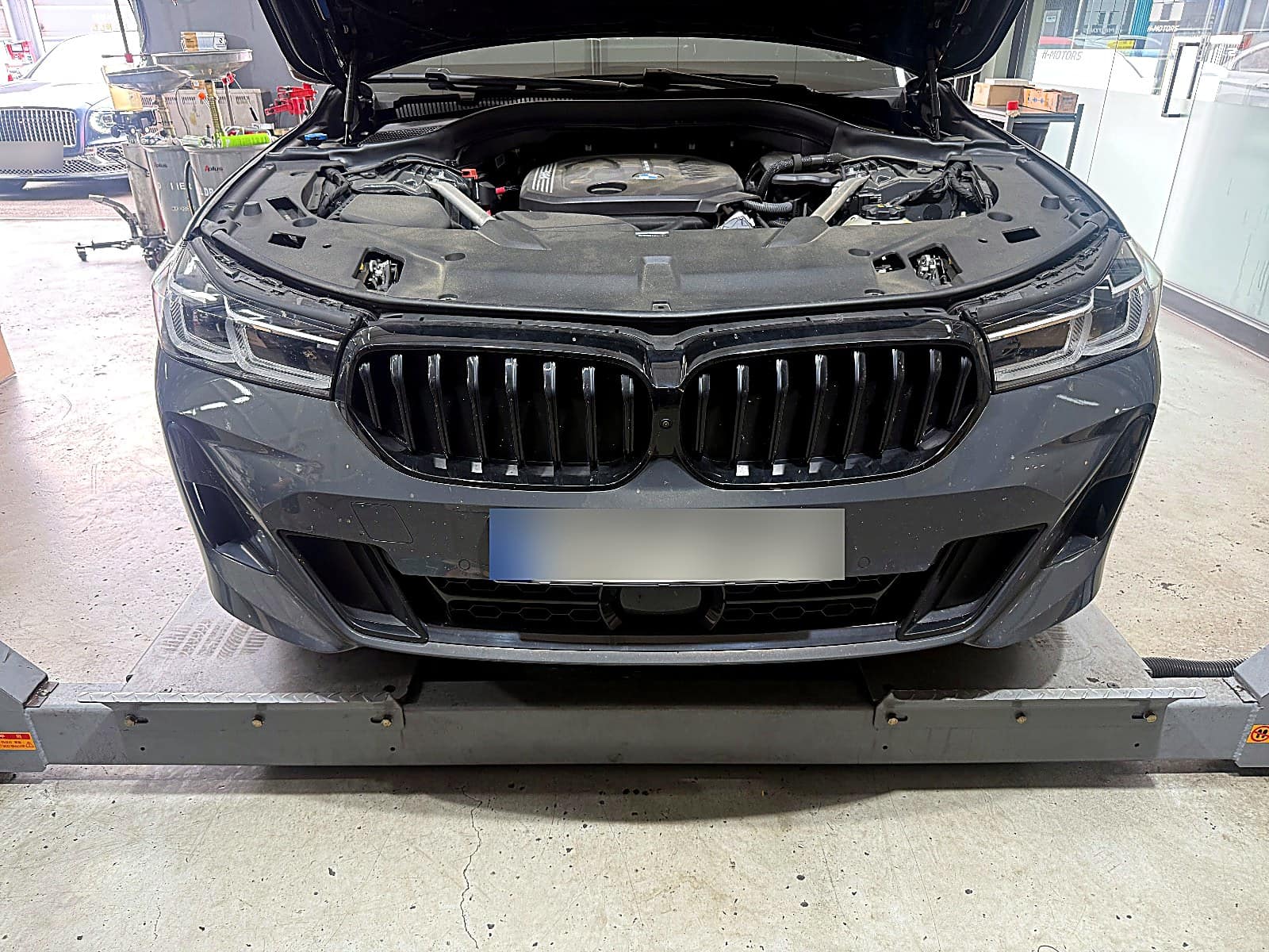 순천 H모터스 리프트에 올라간 진회색 BMW 6시리즈 GT 정면, 보닛을 연 상태
